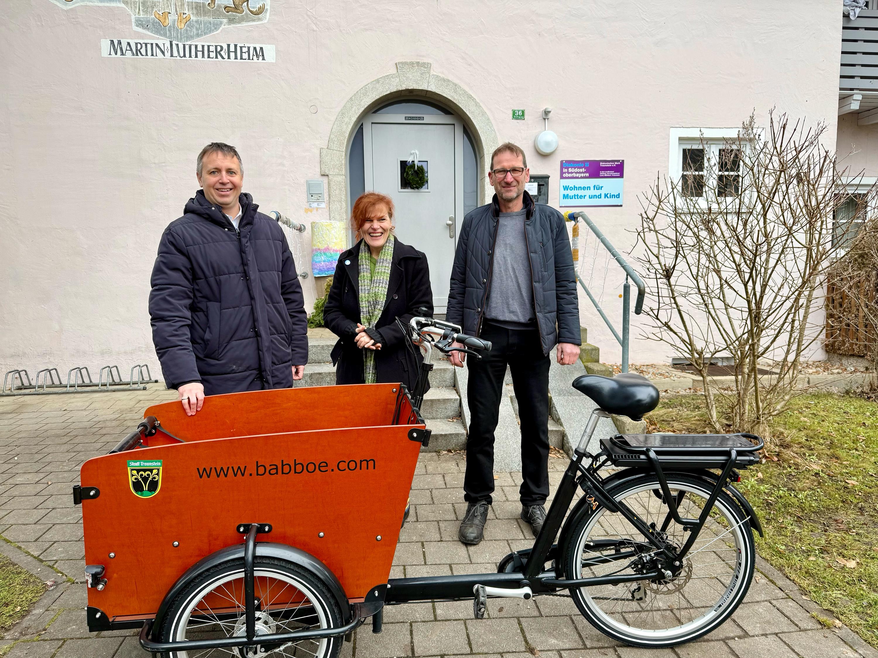 Strahlende Gesichter im „Haus am Triftweg“: Oberbürgermeister Dr. Christian Hümmer (links) und der Fuhrparkleiter der Stadt Traunstein, Hermann Mitterer (rechts), haben ein Lastenrad an Veronika Kecht, Leiterin der Caritas-Einrichtung übergeben. (Foto © Große Kreisstadt Traunstein)