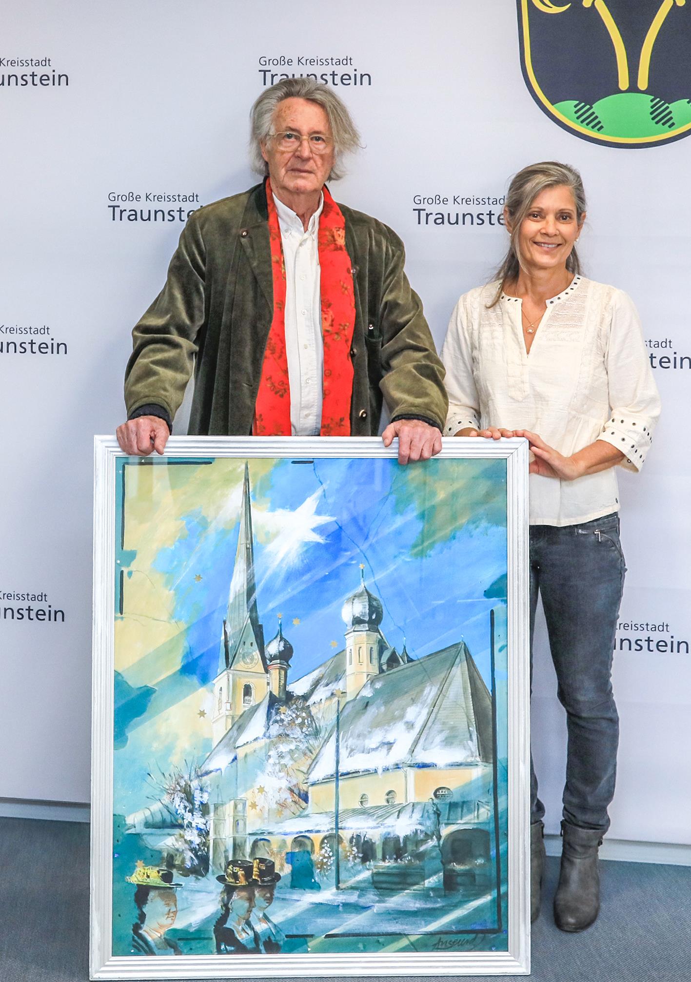 Künstler Walter Angerer d. J. und Cornelia Seehuber aus Taching am See bei der Übergabe des Hauptpreises der Adventskalenderaktion 2026 – ein Origi-nalgemälde des Traunsteiner Künstlers. (© Große Kreisstadt Traunstein)