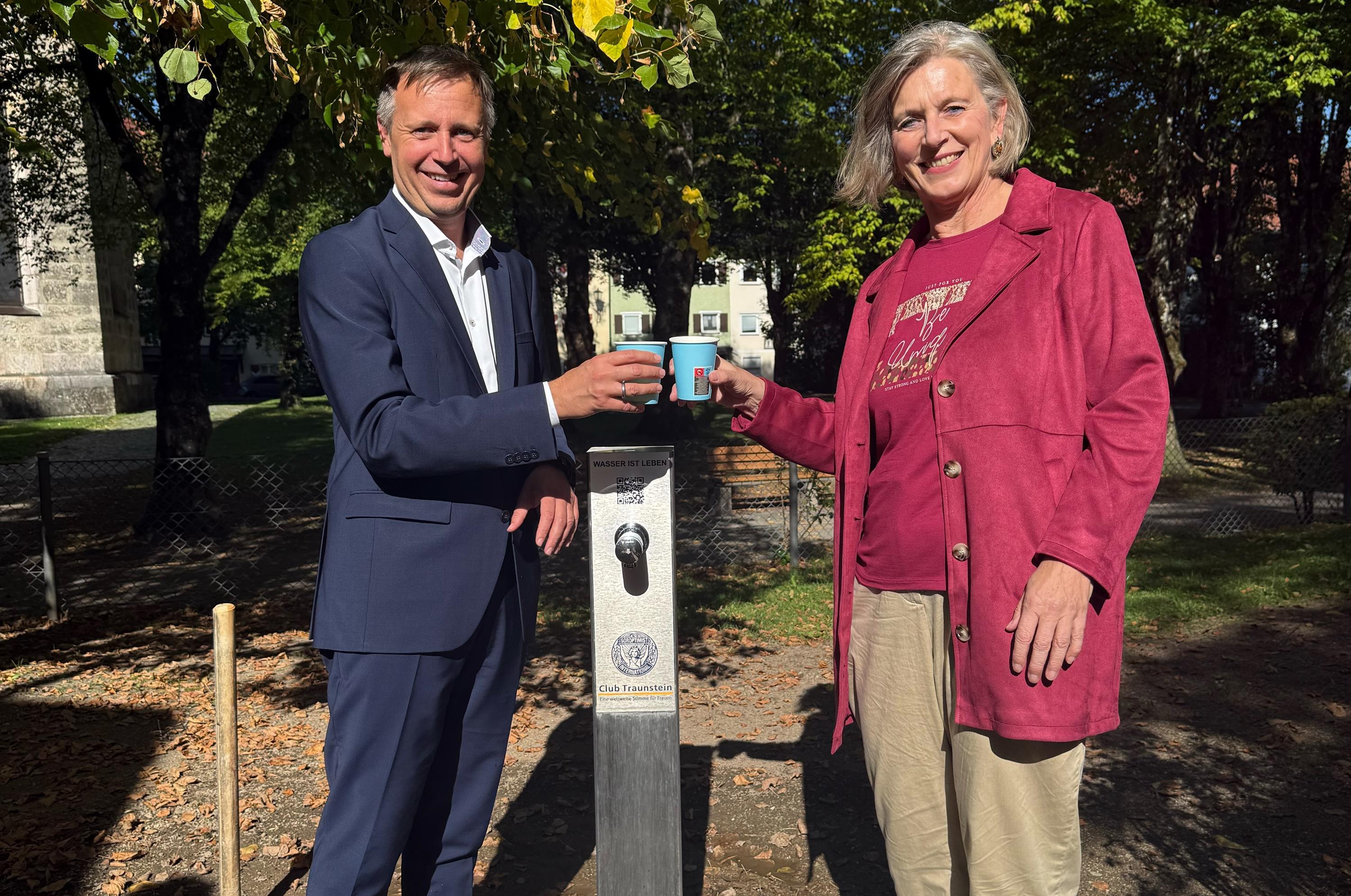 Ein Schluck kühles sauberes Wasser – aus und auf den neuen Trinkwasserbrunnen: Oberbürgermeister Dr. Christian Hümmer (links) und Clubpräsidentin Konstanze Reichert-Kegel stießen am Spielplatz in der Au auf das Geschenk des Soroptimist International Club Traunstein an. (Foto © Carola Westermeier)